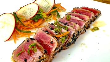 A plate of sliced tuna with sesame seeds, green onions, and radish slices.
