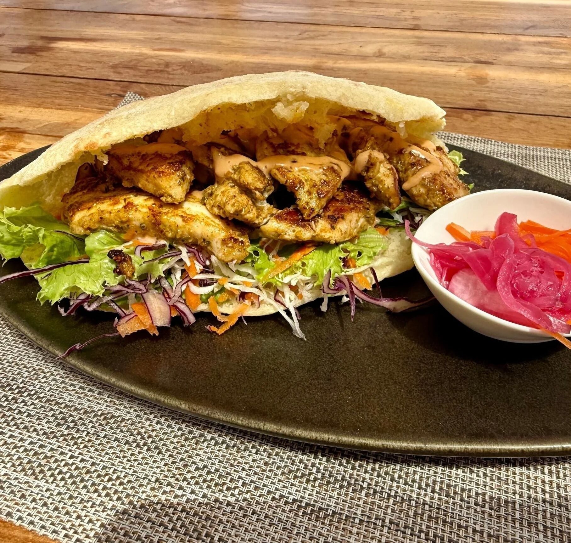 Un plato con pollo a la parrilla, ensalada y verduras encurtidas.