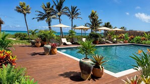 A poolside area with lounge chairs, umbrellas, and potted plants. - Windward Mayreau Resort (Mayreau Island)