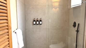 Une douche moderne avec une porte en verre, un pommeau de douche à main et trois bouteilles de shampoing.