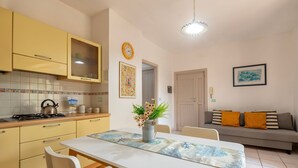 A kitchen with yellow cabinets, a white table, and a gray sofa. - Sardinia Re - Lido 125 (Alghero)