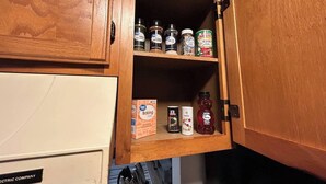 Un meuble en bois doté d’étagères où sont rangés divers articles de cuisine, comme du bicarbonate de soude, du miel et des épices.
