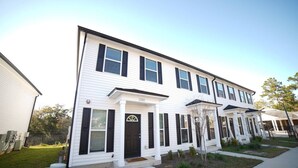 A two-story residential building with a front porch, a garage, and a small front yard.