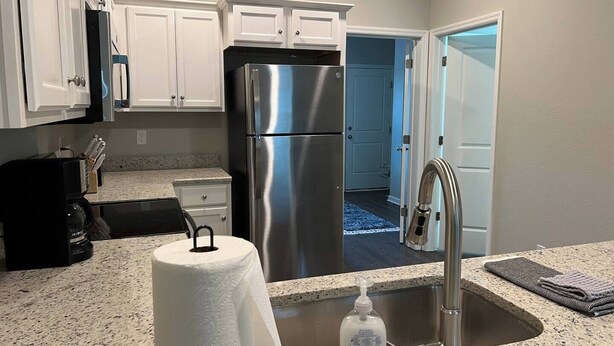 A kitchen with white cabinets, a stainless steel refrigerator, a coffee maker, and a sink with a soap dispenser.
