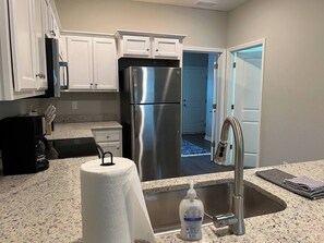 A kitchen with white cabinets, a stainless steel refrigerator, a coffee maker, and a sink with a soap dispenser.