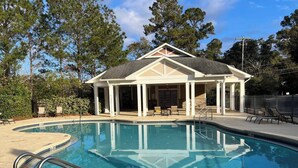 A swimming pool with a covered pavilion, lounge chairs, and a clear sky.