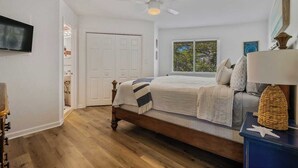 A bedroom with a bed, a ceiling fan, a window, and a TV.