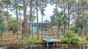 A lakeside cabin with a dock, surrounded by tall trees and a small pond. - For the Birds- relax on the lagoon! (Alligator Point)