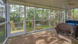 A covered outdoor area with a wicker chair and a blue sofa, large glass doors, and a view of a wooded area. - For the Birds- relax on the lagoon! (Alligator Point)
