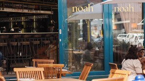 An outdoor seating area with wooden tables and chairs, a large white umbrella, and a storefront with the name 'noah'. - Charles Hope Boutique Hometel (Cape Town)