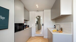 A modern kitchen with white cabinets, a black microwave, and a countertop with a coffee maker and croissants. - Charles Hope Boutique Hometel (Cape Town)