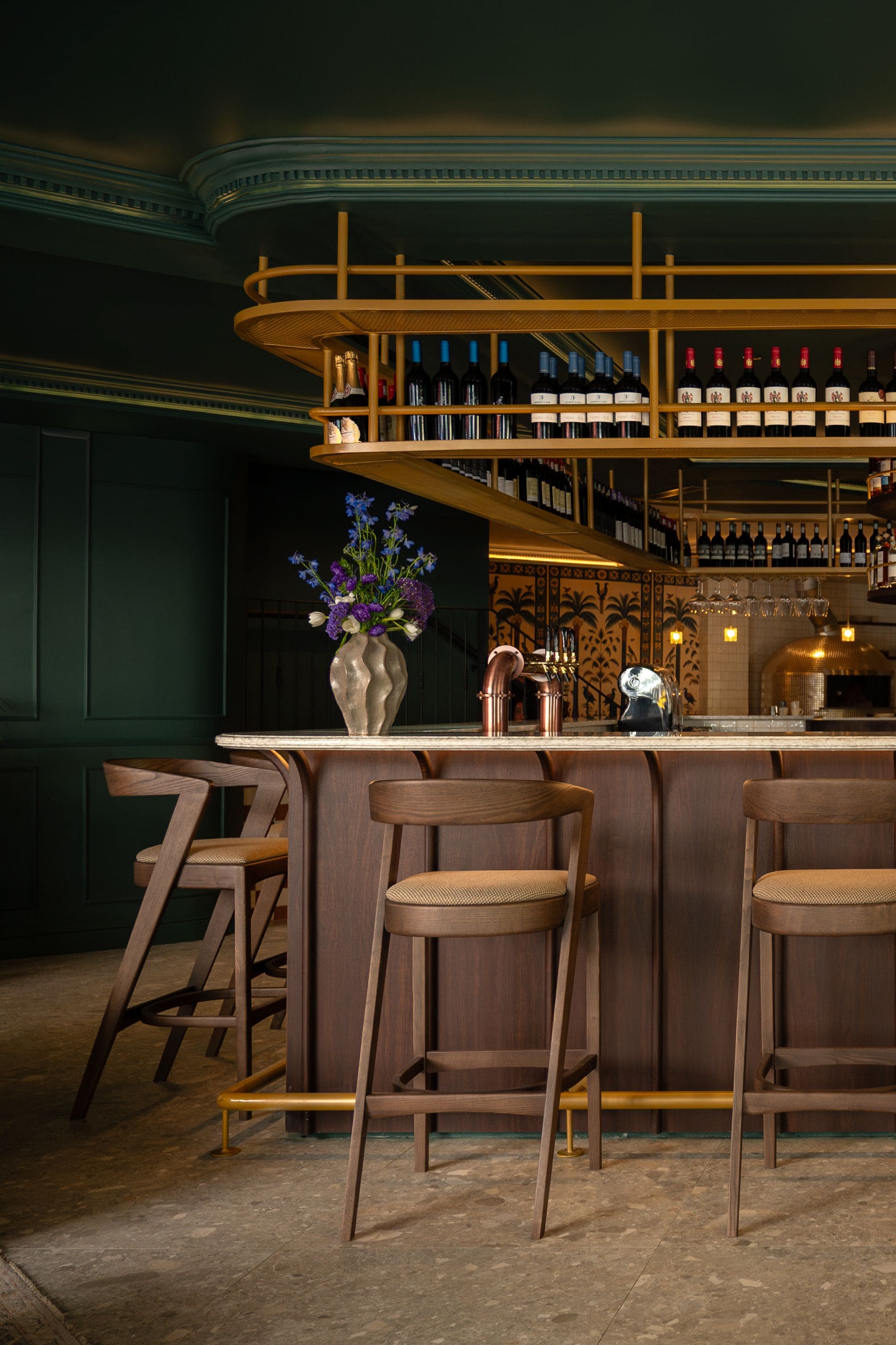 A bar area with wooden chairs, a bar counter, and a wine rack with bottles.