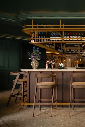 A bar area with wooden chairs, a bar counter, and a wine rack with bottles. - Charles Hope Boutique Hometel (Cape Town)