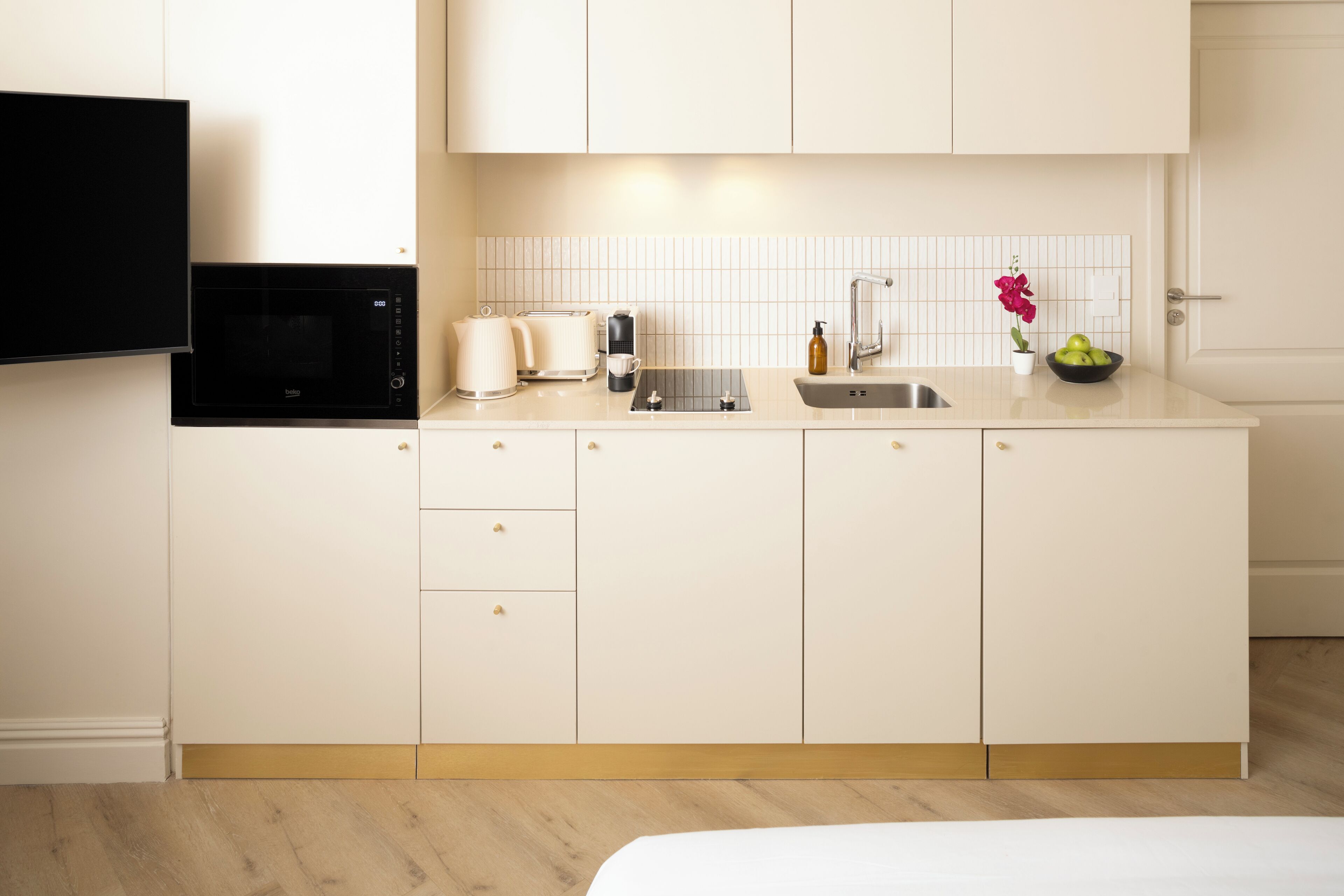 A modern kitchen with white cabinetry, a built-in microwave, a toaster, a sink, and a small vase with flowers.