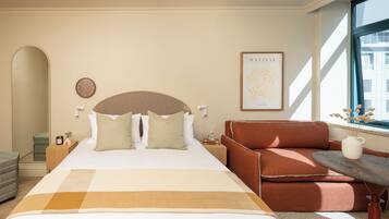 Quarto de hotel com uma cama grande, um sofá, uma mesa pequena, um relógio e um quadro na parede.