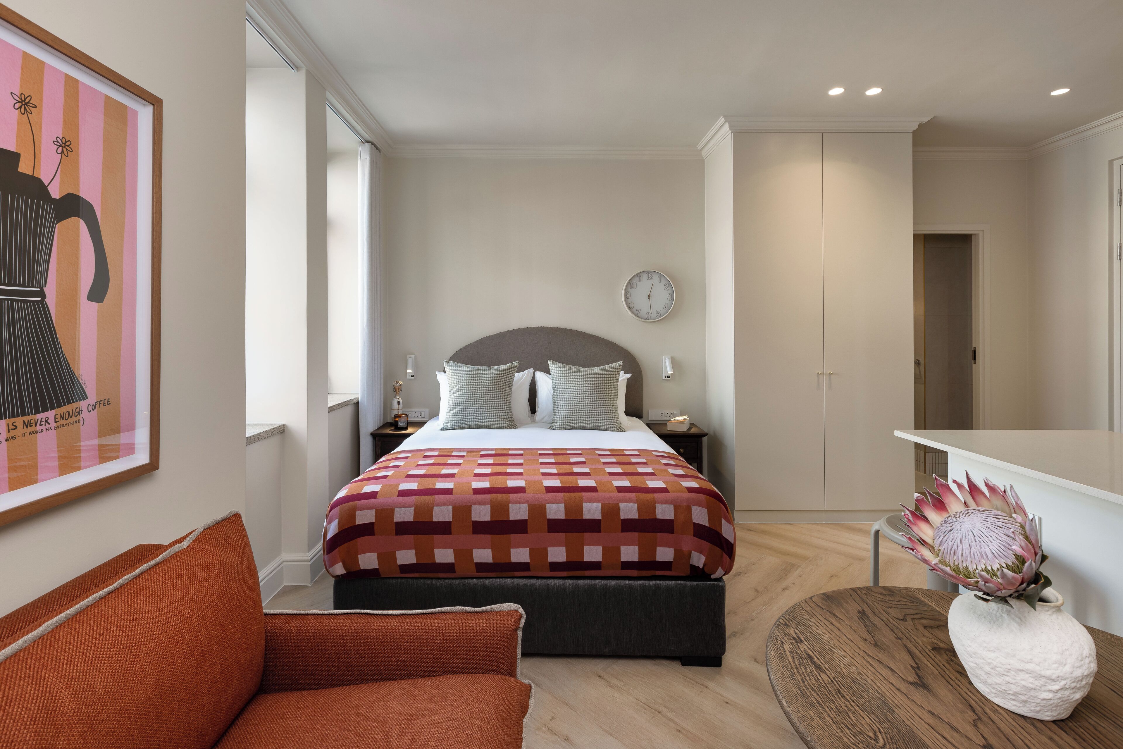 A modern bedroom with a large bed, bedside tables, a clock, and a decorative plant.