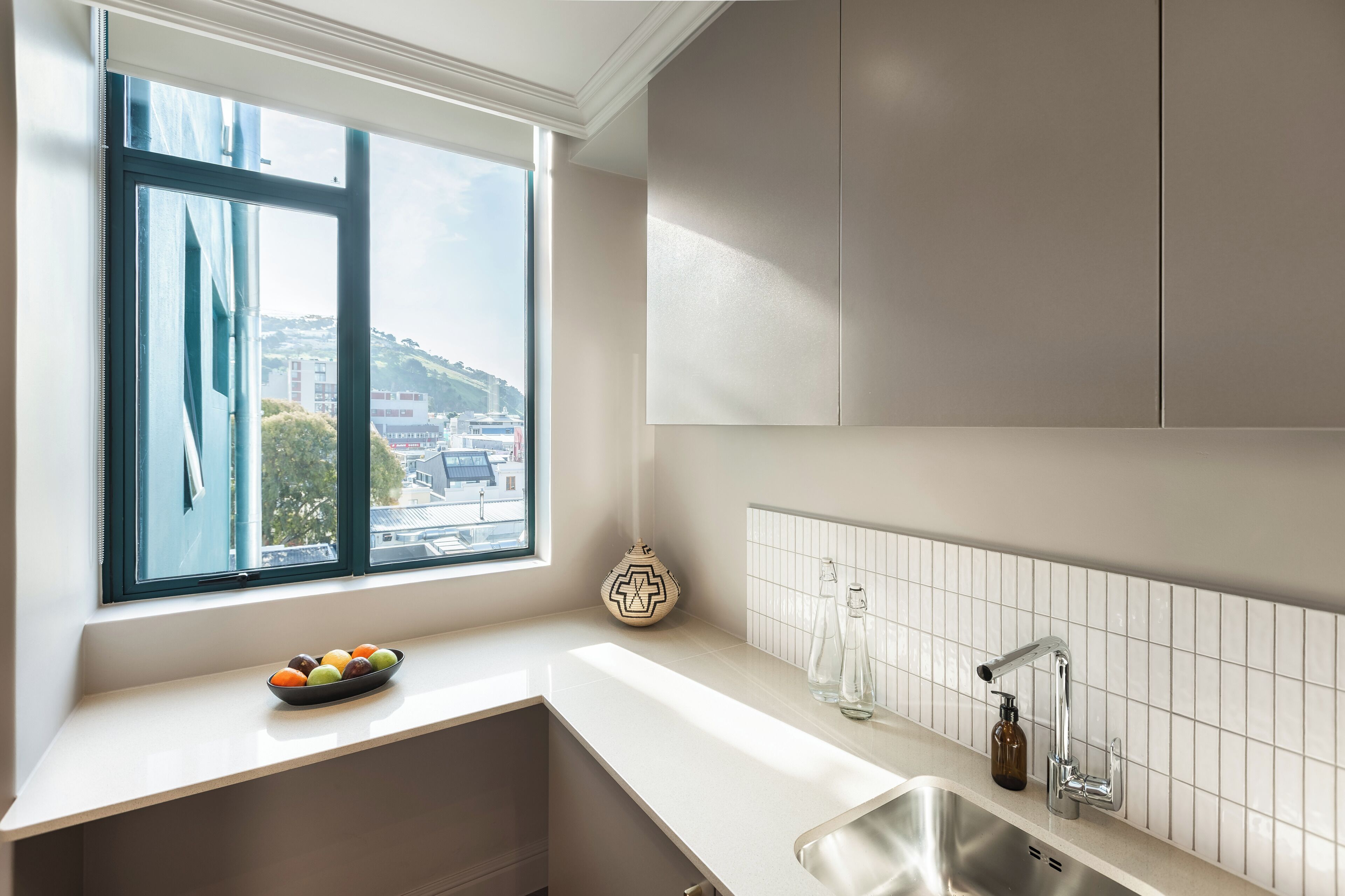 A modern kitchen with a large window, a bowl of fruit on the counter, and a sink with a faucet.