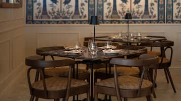 A dining area with round tables, chairs, and a decorative wall with palm trees and birds.