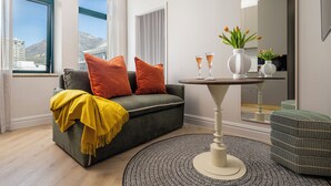 A modern living room with a grey sofa, orange cushions, a yellow throw blanket, a round coffee table, and a mirror reflecting the room. - Charles Hope Boutique Hometel (Cape Town)