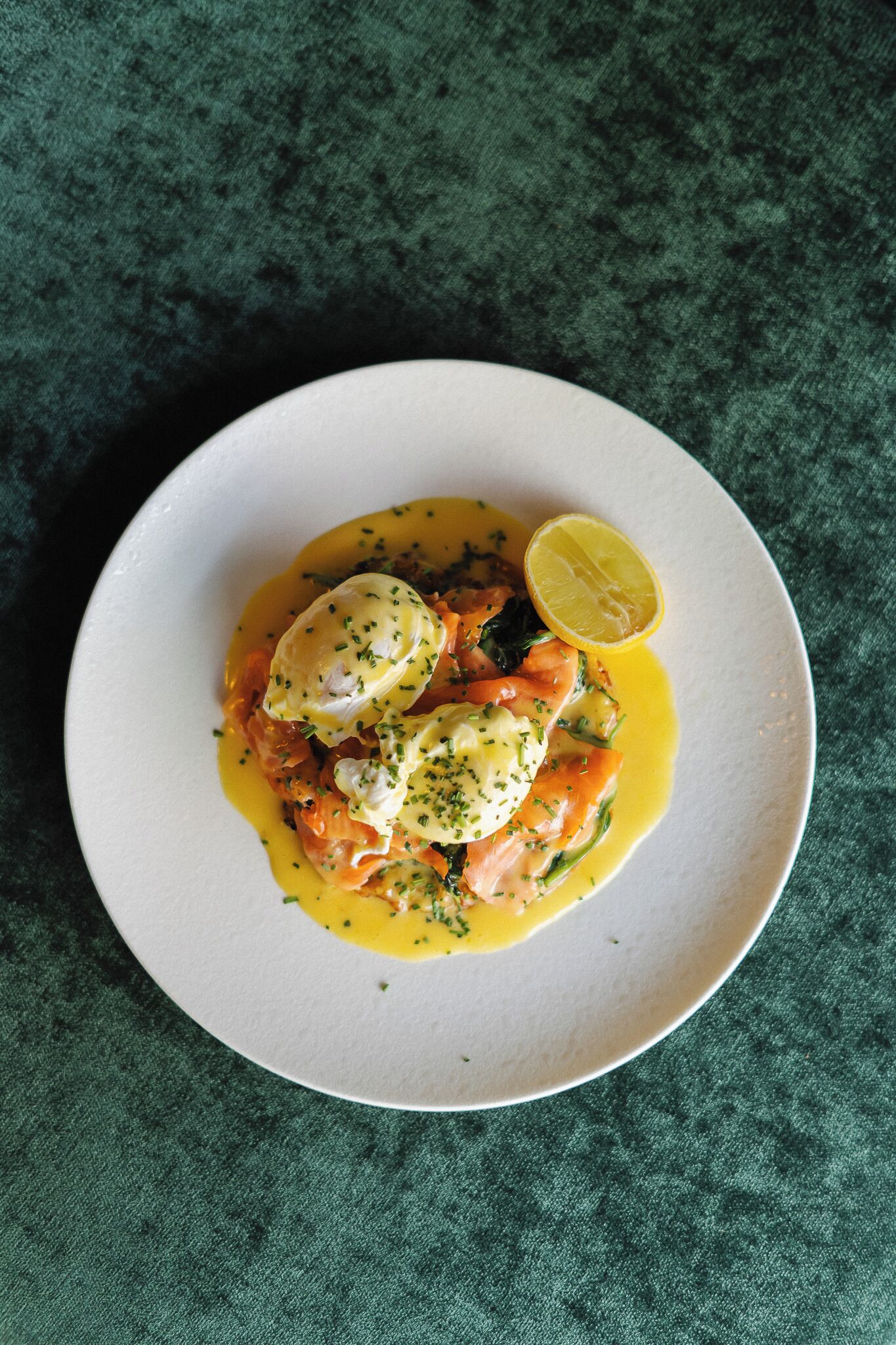 A plate of food with poached eggs, salmon, and a lemon wedge on a textured green background.