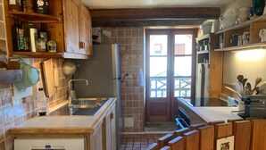 A kitchen with wooden cabinets, a sink, and a dishwasher. There are shelves with bottles and a window with a view. - Large house near the slopes, La Salle-les-Alpes (La Salle-les-Alpes)