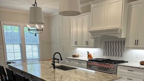 A modern kitchen with white cabinetry, a large granite island, black bar stools, and a stainless steel range hood. - Charming 5-bedroom Masters Rental house in River Oaks  in quaint Evans (Evans)