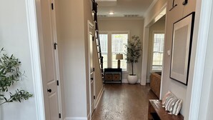 A hallway with wooden flooring, white walls, a staircase, a bench, and a potted plant. - Charming 5-bedroom Masters Rental house in River Oaks  in quaint Evans (Evans)