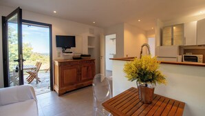 A modern kitchen with a wooden table, a TV mounted above the counter, and a view of the outdoors through a glass door. - Casarone : Havre de paix avec vue sublime sur Calvi, piscine et nature (Calvi)