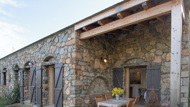 A stone building with a wooden pergola, a table with chairs, and a potted plant. - Casarone : Havre de paix avec vue sublime sur Calvi, piscine et nature (Calvi)
