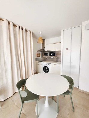 A compact kitchen with a microwave, washing machine, and a hanging light fixture. - Cosy studio - walking distance to beach and pool (Linguizzetta)