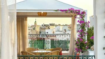 A balcony with wicker furniture, a view of buildings, and a pergola with flowers.