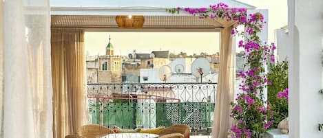 A balcony with wicker furniture, a view of buildings, and a pergola with flowers.