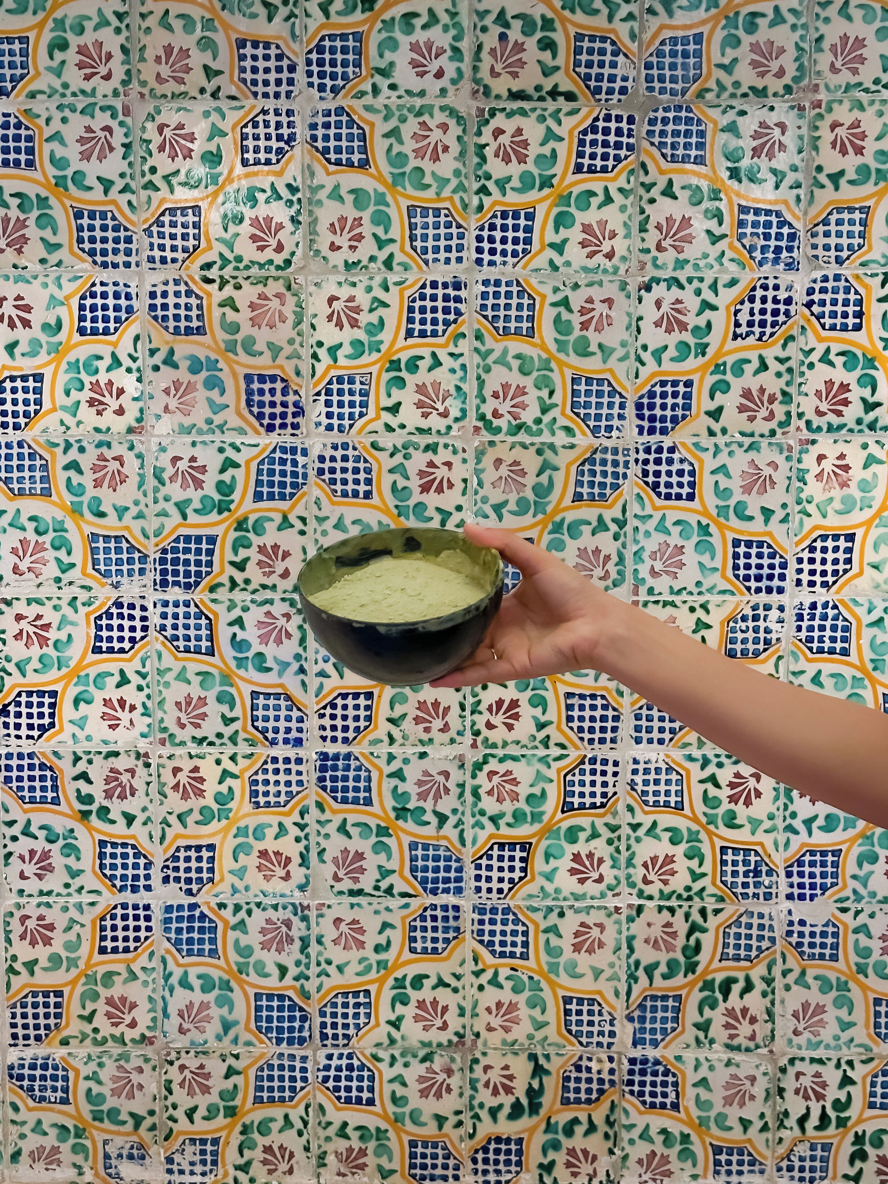 Una mano sosteniendo un cuenco frente a una pared de azulejos decorativos.