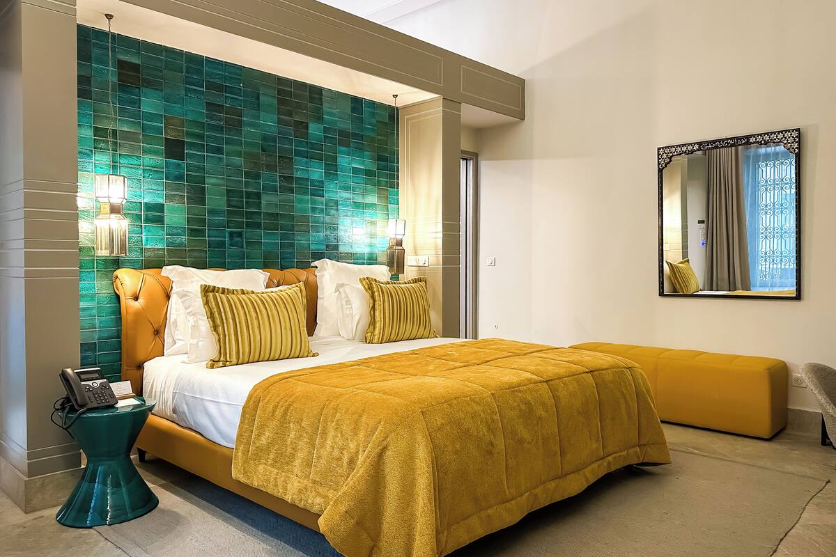A modern hotel room with a large bed, a bedside telephone, and a decorative mirror.