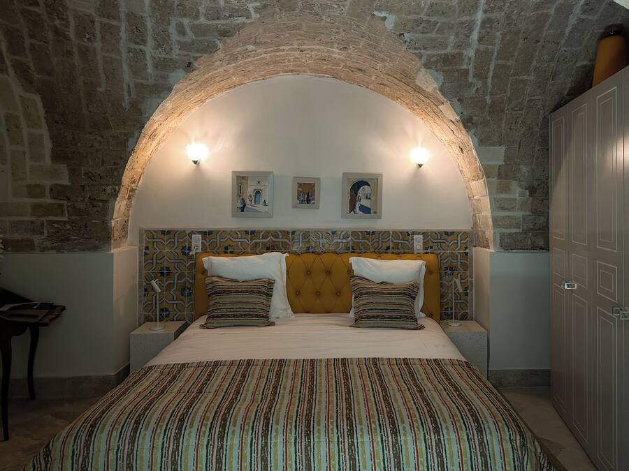 Een slaapkamer met een plafond van natuursteen, een bed met gestreept beddengoed en twee wandlampen.