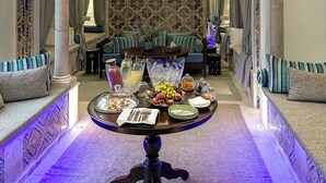 Un salón lujoso con una araña, una mesa de centro redonda con aperitivos y bebidas, y una pared con diseño.