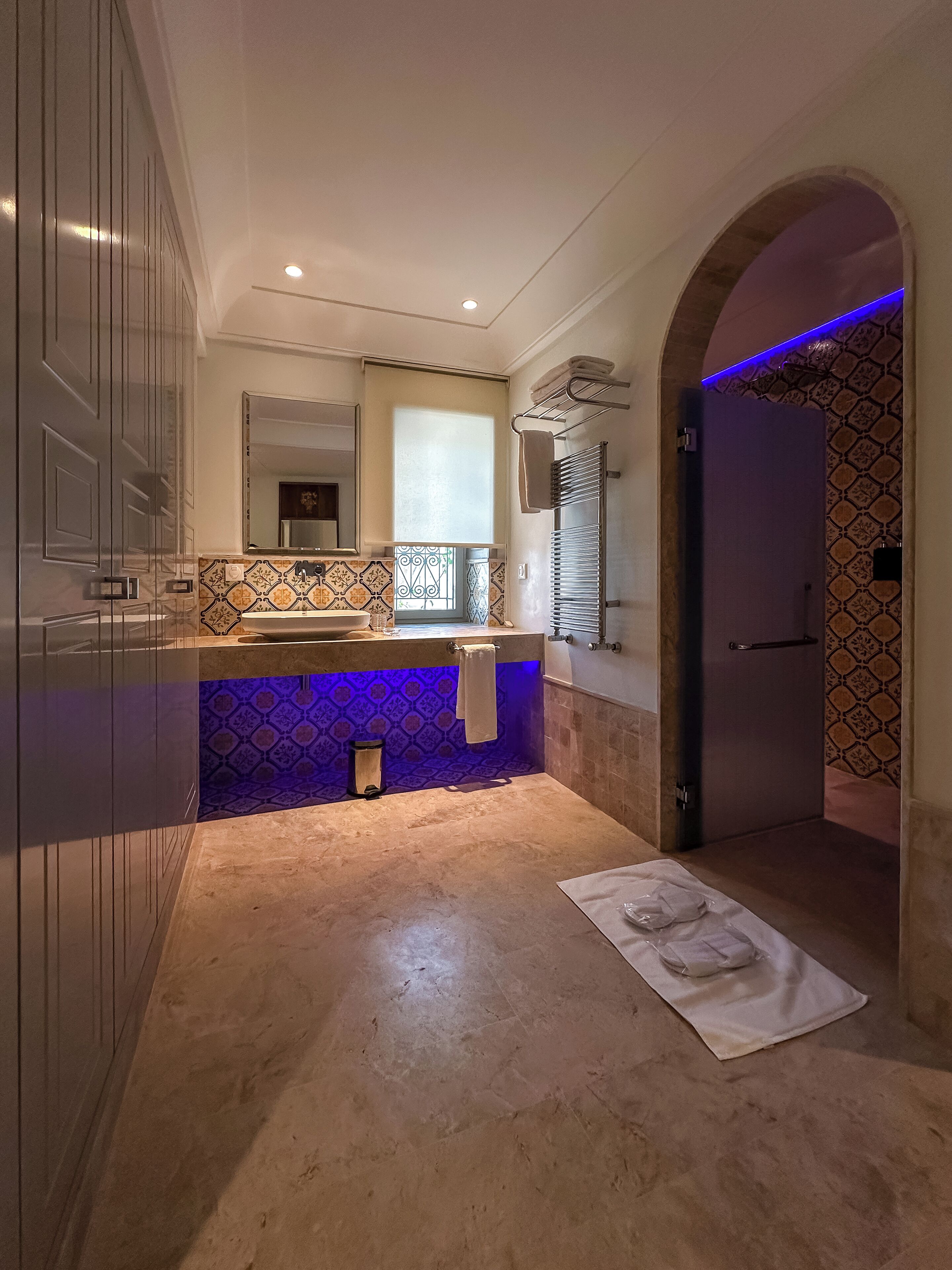 A modern bathroom with a marble floor, a sink with a mirror, and a towel rack.