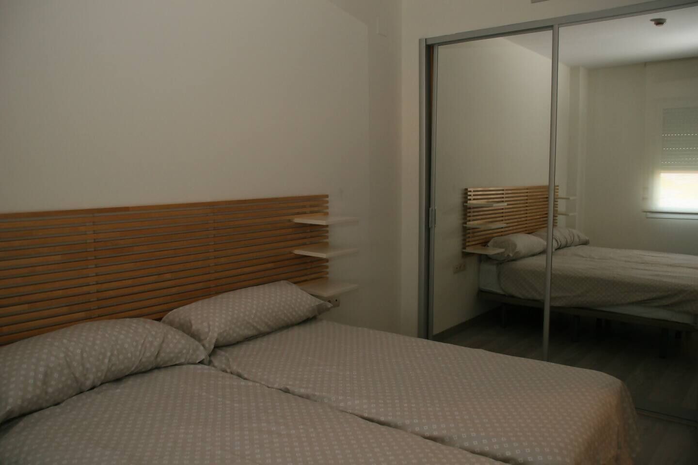 Ein Schlafzimmer mit einem Holz-Kopfteil, einem Bett mit einem gemusterten Überwurf und einer Schiebetür zu einem weiteren Raum.