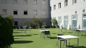 Un área de estar al aire libre con mesas y sillas, rodeada por un edificio con numerosas ventanas.