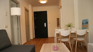 Una sala de estar moderna con un sofá gris, una mesa de comedor de madera con sillas, una lámpara y una puerta negra al fondo.