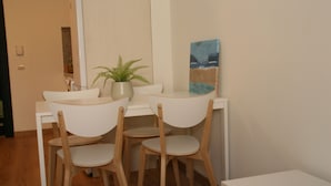 Una piccola zona pranzo con un tavolo bianco, due sedie, una pianta in vaso e un quadro appeso al muro.