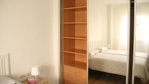 Una camera da letto con un'armadio in legno, un comodino con una lampada e un letto con copripiumino bianco.