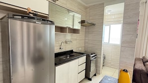 A modern kitchen with a stainless steel refrigerator, a built-in oven, and a black countertop. - Foot in the sand at Maracanã beach II (Praia Grande)