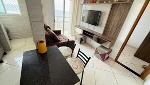 A modern living room with a sofa, a dining table, and a TV mounted on the wall. - Foot in the sand at Maracanã beach II (Praia Grande)