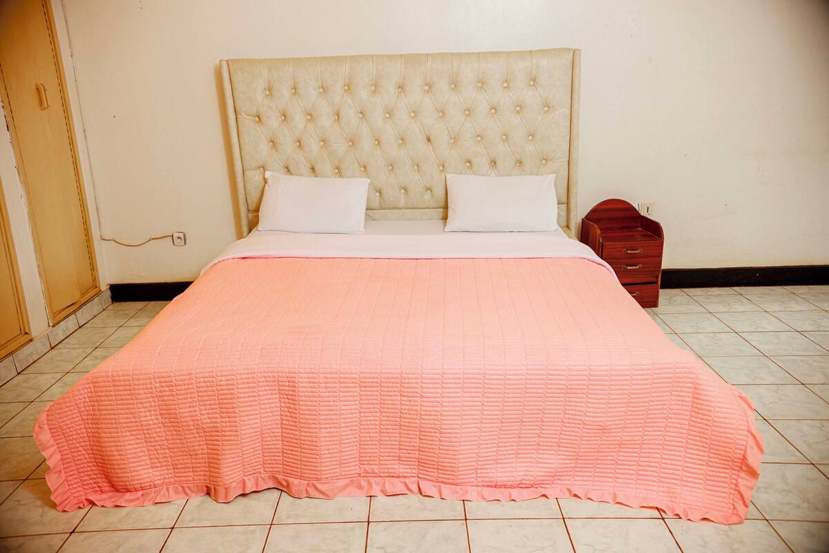 Un lit avec une couverture rose matelassée, une tête de lit capitonnée et deux oreillers blancs.