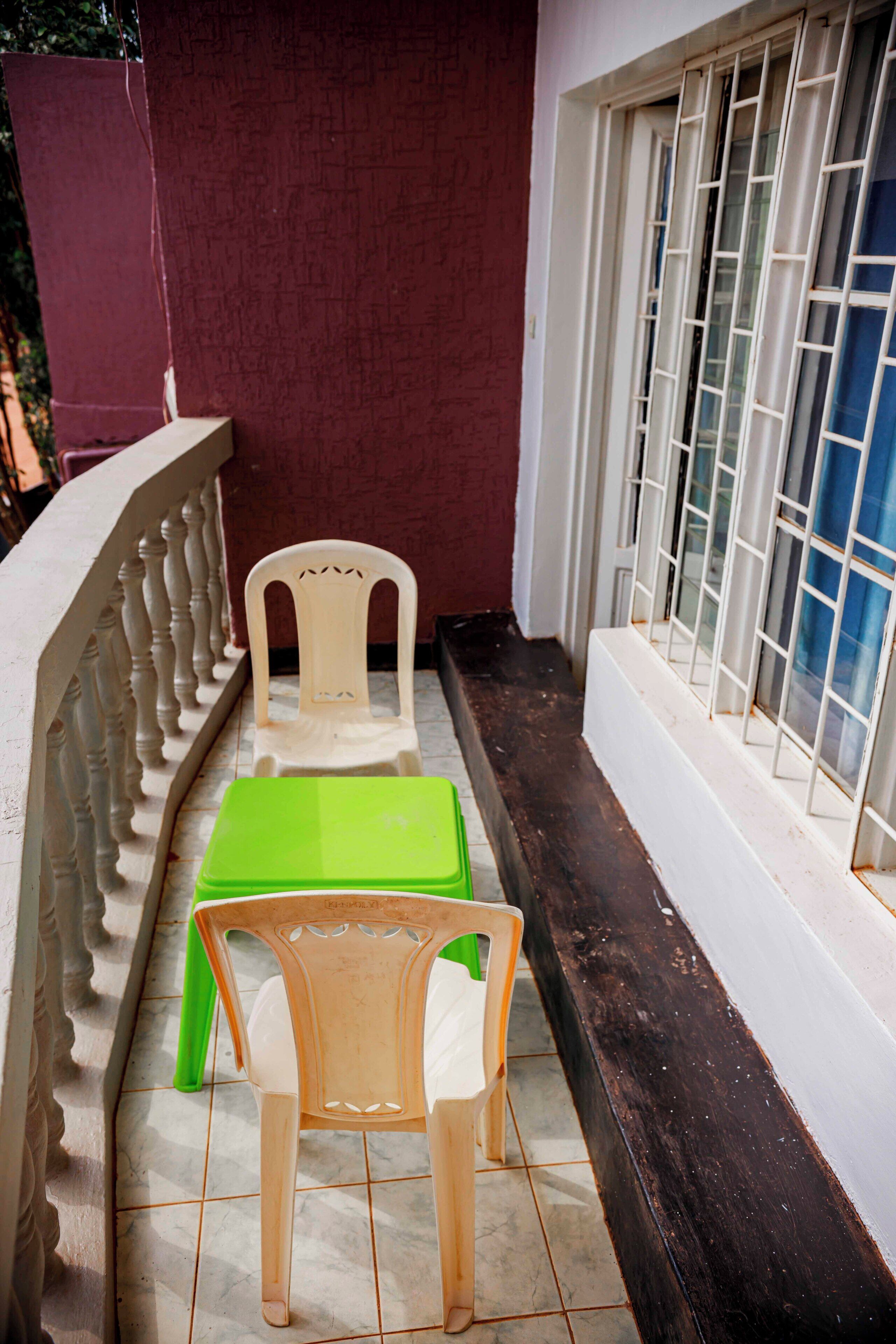 Un étroit couloir extérieur doté d’une balustrade blanche, d’une table verte, d’une chaise blanche et d’une fenêtre avec des barreaux blancs.