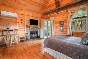 L’intérieur d’une cabane avec une cheminée en pierre, des murs en bois, un lit et un téléviseur.