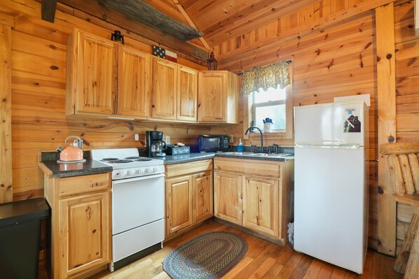 A wooden cabin kitchen with a stove, sink, refrigerator, and cabinets.