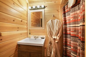 A wooden cabin bathroom with a sink, mirror, robe, and patterned shower curtain.