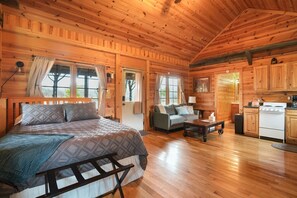 A log cabin with a wooden interior, a bed, a sofa, a dining table, and a kitchen area.